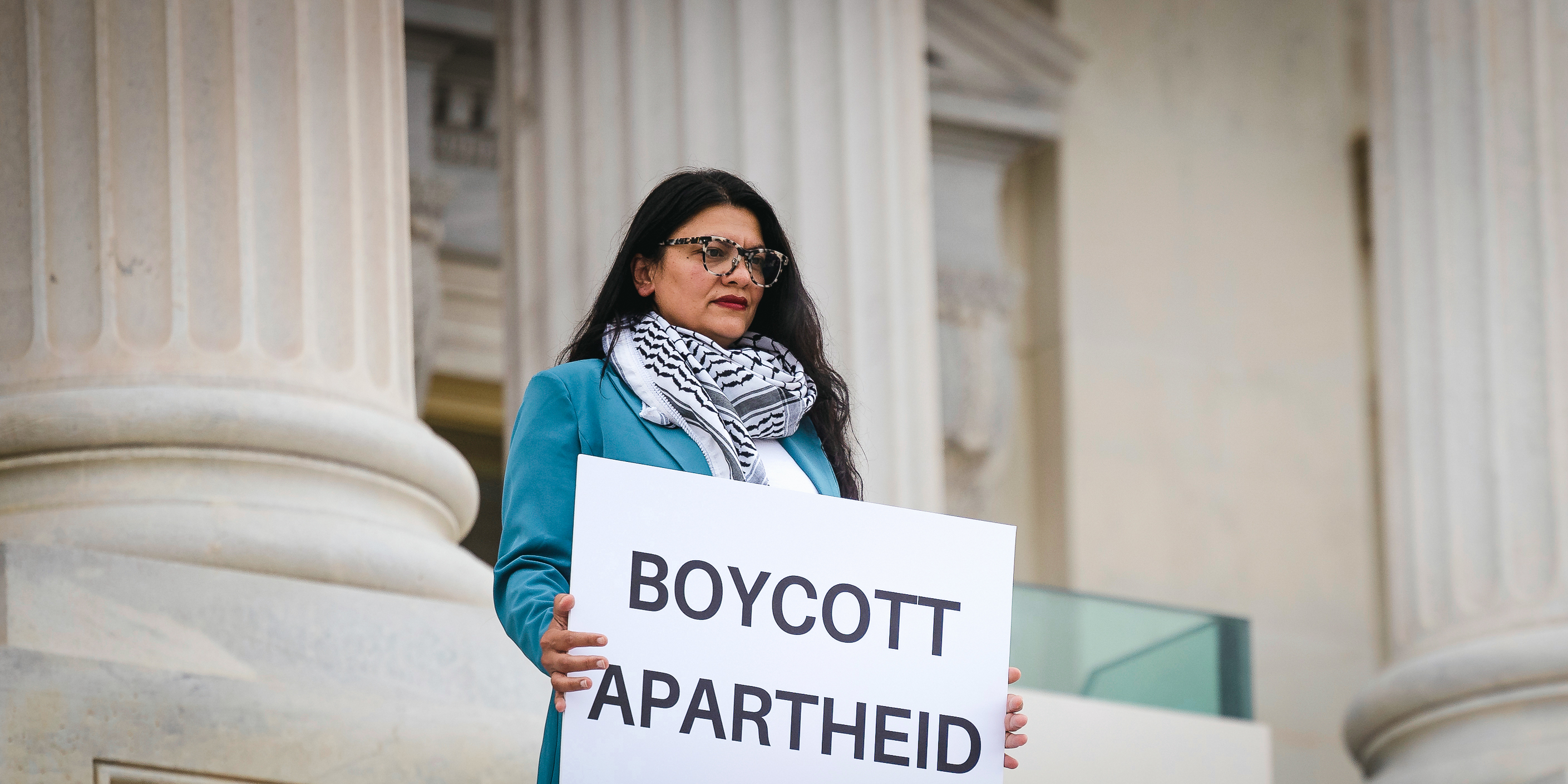 Rep. Rashida Tlaib (D-Mich.) holds a sign that reads "BOYCOTT APARTHEID" while an aide takes a photograph outside the U.S. Capitol July 17, 2023. (Francis Chung/POLITICO via AP Images)