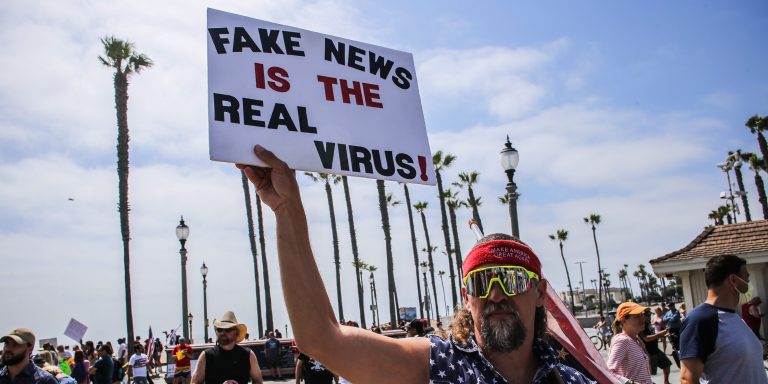 HUNTINGTON BEACH, CALIFORNIA, UNITED STATES - 2020/05/09: A protester holds a placard that says Fake News Is The Real Virus during the demonstration. Citizens staged a protest in front of the Huntington Beach Pier to demand for the reopening of the California economy. (Photo by Stanton Sharpe/SOPA Images/LightRocket via Getty Images)