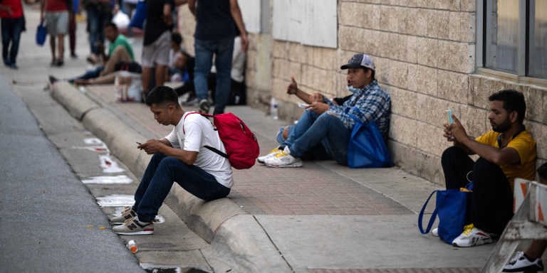 Migrants that arrived from Mexico look at their phones as they wait for transportation near a processing center, in Brownsville, Texas on May 10, 2023. The US on May 11, 2023, will officially end its 40-month Covid-19 emergency, also discarding the Title 42 law, a tool that has been used to prevent millions of migrants from entering the country. (Photo by ANDREW CABALLERO-REYNOLDS / AFP) (Photo by ANDREW CABALLERO-REYNOLDS/AFP via Getty Images)