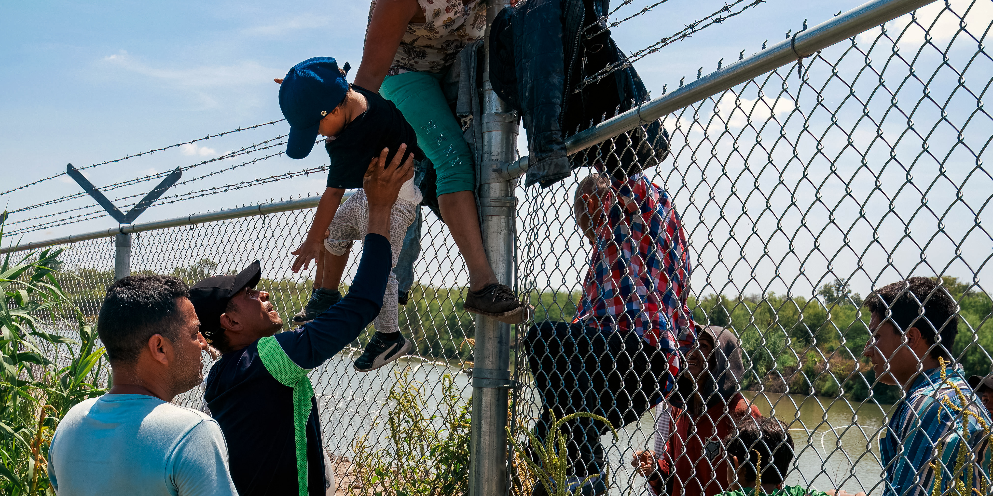 Migrants climb over a barbed wire fence after crossing the Rio Grande into US from Mexico, in Eagle Pass, Texas on August 25, 2023. (Photo by SUZANNE CORDEIRO / AFP) (Photo by SUZANNE CORDEIRO/AFP via Getty Images)