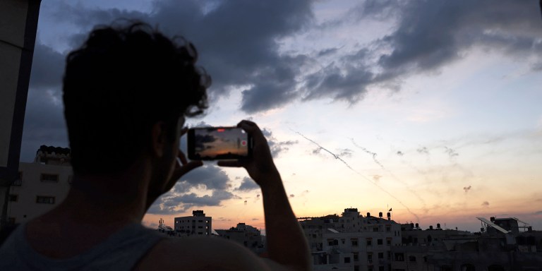 A man records a video with his mobile phone of rockets being fired from Gaza City towards Israel on October 7, 2023. Dozens of rockets were fired from the blockaded Gaza Strip towards Israel on October 7, 2023, an AFP journalist in the Palestinian territory said, as sirens warning of incoming fire blared in Israel. (Photo by MOHAMMED ABED / AFP) (Photo by MOHAMMED ABED/AFP via Getty Images)