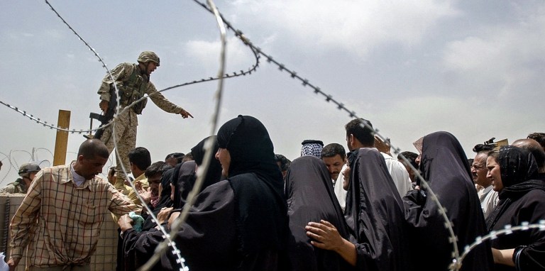 A US marine points as he tells a crowd of men and women to move the line back outside the Abu Ghraib prison 12 May 2004. Hundreds of Iraqis crowd everyday outside the detention center in an effort to find news about their loved ones and to hopefully get an appointment slip for the near future to visit them.  AFP PHOTO/Roberto SCHMIDT / AFP / ROBERTO SCHMIDT        (Photo credit should read ROBERTO SCHMIDT/AFP via Getty Images)
