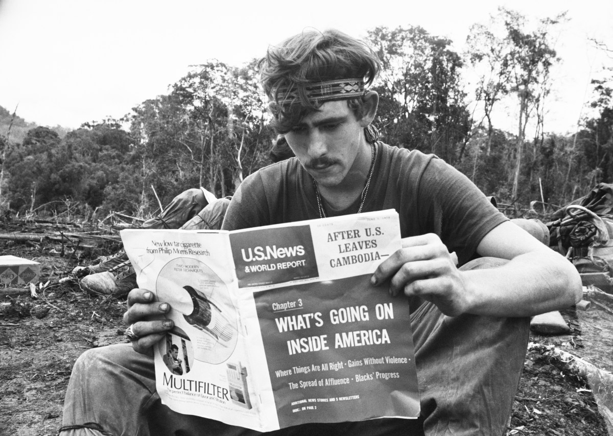 (Original Caption) June 29, 1970 - Waiting for a helicopter to carry his unit back into South Vietnam, a 1st Air Cavalry Division GI reads a magazine (U.S. News and World Report) at a firebase inside Cambodia. The magazine deals heavily with the operation he has been personally involved in the past two months trudging through the Cambodian jungles looking for Viet Cong and North Vietnamese cache areas. He wears a headband which gained popularity with GI's around Vietnam.